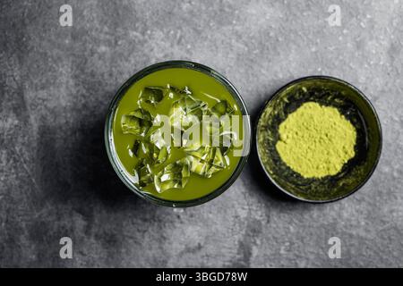 Nahaufnahme von eisgekühltem Matcha-Grüntee auf dem Glas und Matcha-Grüntee-Pulver in der Schüssel auf dem schwarzen Tisch. Draufsicht Stockfoto