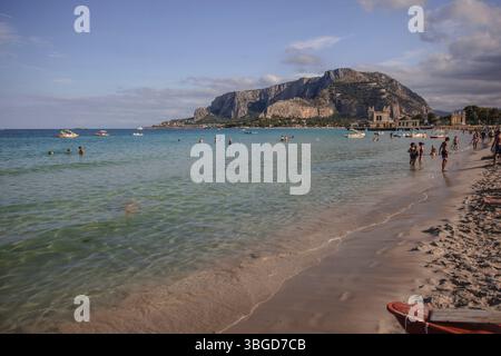 Mondello, Italien 1. Januar 2025: Touristen, die an einem sonnigen Sommertag im klaren Wasser des Strandes mondello baden, mit monte pellegrino im Hintergrund Stockfoto