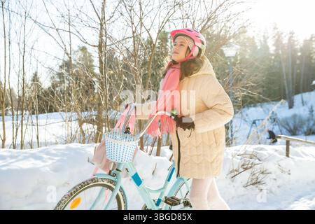 Tween geht mit ihrem Fahrrad nach Hause an einem sonnigen Wintertag in einem finnischen Vorort. Schnee auf dem Boden, ein echter Moment des nordischen Alltags. Stockfoto