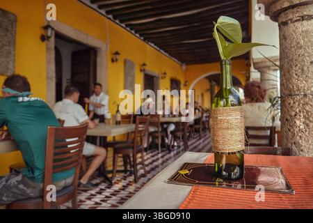 Valladolid, Mexiko 1. Januar 2025: Leere Weinflasche mit Seilen und Pflanzenblättern als Herzstück auf einem Restauranttisch in valladolid, mex Stockfoto