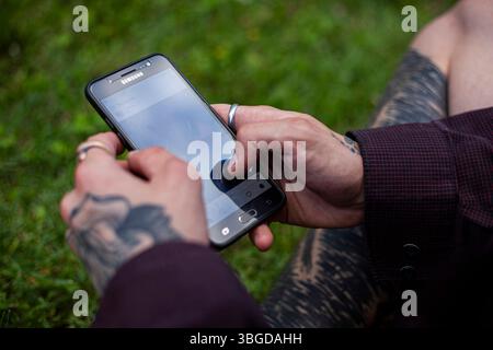 Bologna, Italien 1. Januar 2025: Tätowierter Mann mit Handy, der im Freien in sozialen Medien surft Stockfoto