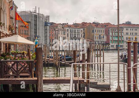 Venedig, Italien 1. Januar 2025: Gondeln, die neben einer Restaurantterrasse mit schwenkender italienischer Flagge in einem Kanal von venedig vertäut sind Stockfoto