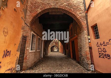 Ferrara, Italien 2. Januar 2025: Backsteinbögen verbinden Gebäude entlang einer Gasse in ferrara, italien, mit Graffiti und Kopfsteinpflaster Stockfoto
