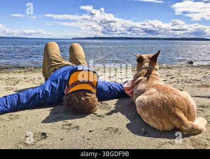 San Francisco, Kalifornien, USA – 15. Mai 2025: Ein Hund und eine Person liegen nebeneinander an einem Sandstrand und beobachten friedlich die Wellen. Stockfoto
