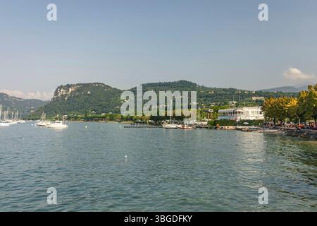 Gardasee, Italien 3. Januar 2025: Malerischer Blick auf den gardasee mit Segelbooten, Gebäuden und Bergen unter blauem Himmel in italien Stockfoto