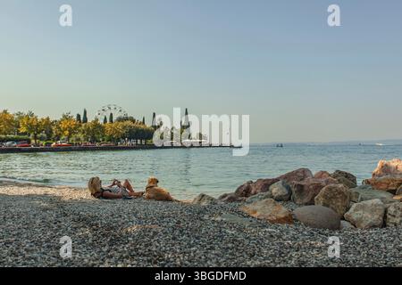 Gardasee, Italien 3. Januar 2025: Touristen genießen Sommerferien mit ihrem Hund am Kiesstrand von bardolino, gardasee, italien Stockfoto