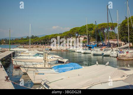 Gardasee, Italien 3. Januar 2025: Weiße Boote legen am gardasee an, wo sich Touristen am Ufer in bardolino, italien, entspannen Stockfoto