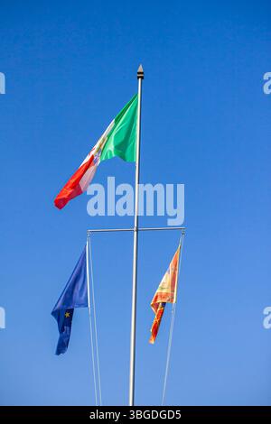 Gardasee, Italien 3. Januar 2025: Im klaren blauen Himmel des gardasees, italien, der europäischen union und venetiens winken die Flaggen italiens, der europäischen union und der Region venetien Stockfoto