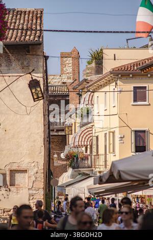 Gardasee, Italien 3. Januar 2025: Touristen wandern und shoppen in bardolino am gardasee, italien, mit italienischer Flagge Stockfoto
