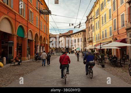 Modena, Italien 1. Januar 2025: Menschen fahren und spazieren im Stadtzentrum von modena, mit farbenfrohen Gebäuden und Cafés im Freien Stockfoto