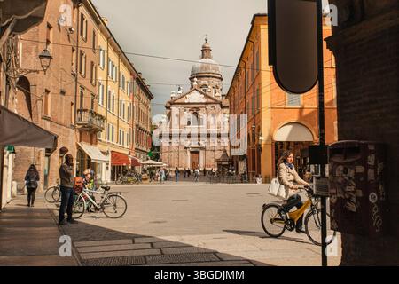 Modena, Italien 1. Januar 2025: Frau radelt im Zentrum von modena mit der Kirche chiesa di san biagio im Hintergrund an einem sonnigen Tag Stockfoto