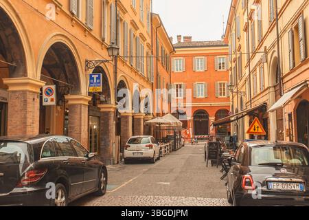 Modena, Italien 1. Januar 2025: Enge Straße in modena, italien, die den architektonischen Charme der Stadt mit parkenden Autos und Restaurants im Freien zeigt Stockfoto