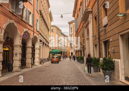 Modena, Italien 1. Januar 2025: Ein Einkaufsbummel durch eine kopfsteingepflasterte Straße mit bunten Gebäuden und Topfpflanzen im historischen Stadtzentrum von Stockfoto