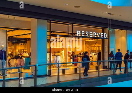 Innenraum eines RESERVIERTEN Modegeschäfts mit Schaufensterpuppen, Kleiderständern und heller Branding, sichtbar durch die Glasfassade im Einkaufszentrum. Konzept von Stockfoto