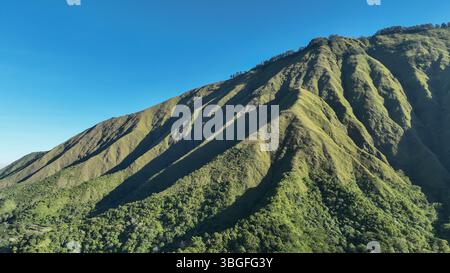 Eine Nahaufnahme der steilen, grünen Bergrücken von Sembalun, wo Sonnenlicht und Schatten die einzigartigen Konturen und wilde Schönheit dieser vulkanischen Landschaft offenbaren. Stockfoto
