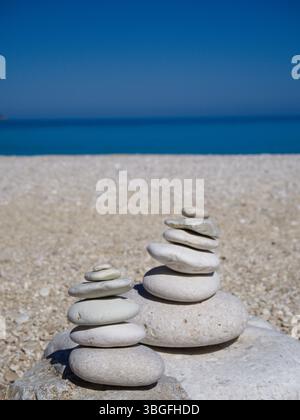 Ausgewogene weiße Steine an einem Strand mit Meer und Sand im Hintergrund. Stockfoto