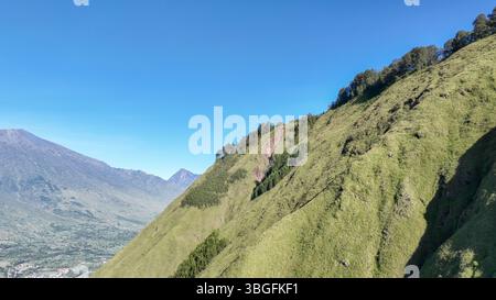 Von Sembalun aus erstreckt sich der Blick über steile, grasbewachsene Hügel bis zu entfernten Vulkangipfeln. Die unberührte Landschaft ist perfekt für Wanderungen und Naturliebhaber Stockfoto
