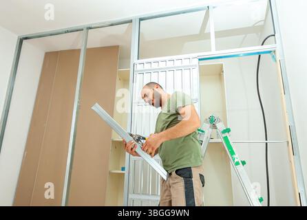 Handyman cutting metal profiles for installing plasterboard walls in a house undergoing renovation, using metal studs and tracks to ensure precision in construction and design Stockfoto