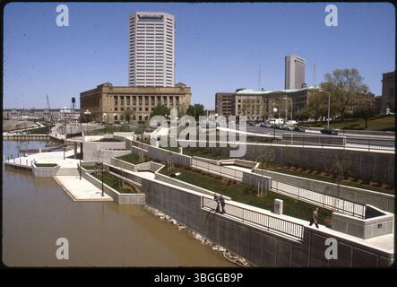 Ein Blick nach Norden auf den Battelle Riverfront Park entlang des Scioto River, der am 15. April 1983 eröffnet wurde. Die Szene umfasst das Joseph P. Kinneary U.S. Courthouse, das AEP Building, die Riverside Plaza, die Columbus Central Police Station, das Nationwide One Building und das Ohio Penitentiary in der Ferne. Stockfoto