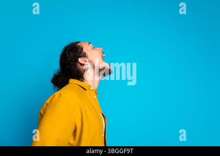 Stilvoller junger Mann in gelbem Hemd, der sich dynamisch und ausdrucksstark vor leuchtendem blauem Hintergrund posiert Stockfoto