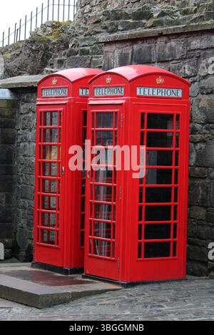 Drei ikonische rote britische Telefondosen stehen neben einer Steinmauer in Edinburgh, Schottland, und symbolisieren den Vintage-Charme und das britische Straßenkultur. Stockfoto