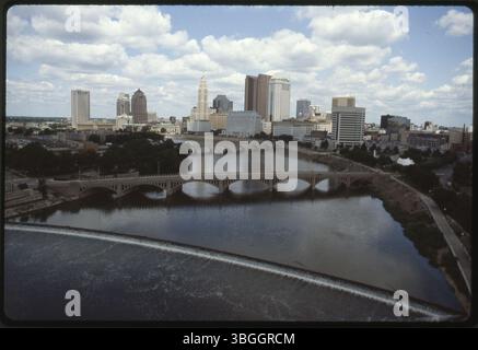Diese aus der Vogelperspektive datiert 1992 und zeigt die Innenstadt von Columbus mit Blick nach Nordosten über den Scioto River. Franklinton erscheint auf der linken Seite, und die zentrale Skyline der Stadt ist auf der rechten Seite zu sehen. Die Town Street Bridge und die Main Street Bridge erstrecken sich über den Fluss, mit einem niedrigen Damm südlich der Main Street Bridge. Stockfoto
