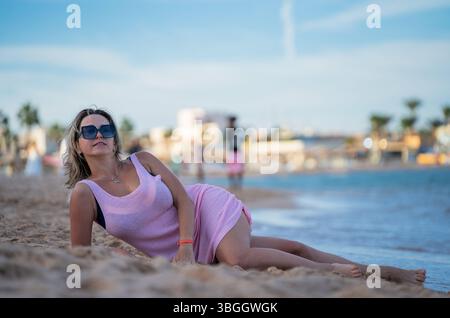 Frau, die am Strand in rosafarbenem Kleid liegt und ihren Urlaub genießt Stockfoto