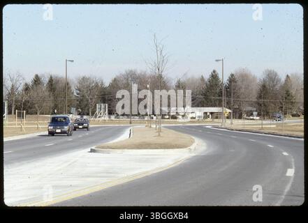 Dieses Foto aus dem Jahr 1988 zeigt eine geteilte Straße mit zwei Fahrspuren in jeder Richtung, die im Mittelstreifen baumlose Bäume zeigt. Die Straße bleibt unbekannt, aber das Bild zeigt ein typisches Vorort- oder Stadtbahnlayout. Stockfoto