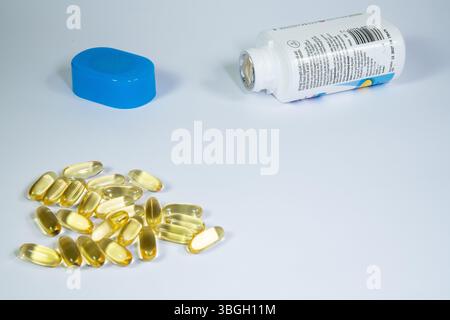 Verstreute Kabeljau Leberöl Kapseln mit Behälter und Deckel im Hintergrund auf weißer Oberfläche, Gesundheits- und Wellness-Konzept. Stockfoto