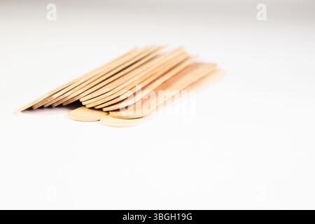 Ein Haufen medizinischer Zunge-Depressoren aus Holz fiel auf weißem Hintergrund um, verstreute klinische Vorräte. Stockfoto