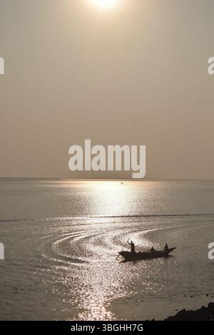 Ein Boot, das auf den goldenen Gewässern des Meghna River driftet und das Wesen des Lebens eines Fischers bei Sonnenuntergang festlegt. Stockfoto
