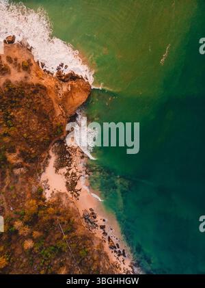 Von oben nach unten blickt man auf die felsige Küste mit Meer, Wellen und warmem Sonnenlicht Stockfoto