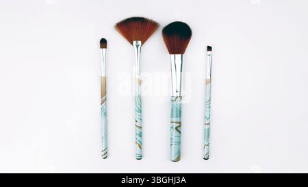 Vier Make-up-Pinsel mit hellblauem und goldenem Marmorgriff auf weißem Hintergrund Stockfoto