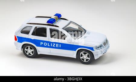 Weißes und blaues deutsches Polizeispielzeugauto parkt auf einem nahtlosen hellen Hintergrund Stockfoto