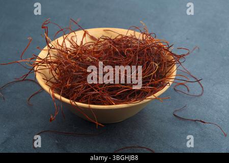 Rote, heiß getrocknete Chilifäden in einer winzigen Holzschale isoliert auf dunklem Hintergrund Stockfoto