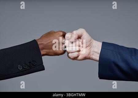 Schwarzer Mann und kaukasischer Mann, die Faustschläge machen, beide tragen Anzüge, Hände treffen sich in der Mitte des Rahmens, symbolisieren unpersönliche Geschäftspartnerschaft und Teamarbeit Stockfoto