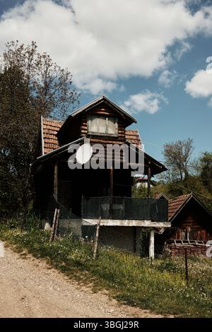 Alte Holzhütte mit Satellitenschüssel und gekacheltem Dach auf einem Hügel in einem abgelegenen serbischen Dorf. Stockfoto