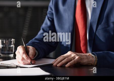 Nahaufnahme der Hände eines kaukasischen Geschäftsmannes mittleren Alters, der Anzug und Armbanduhr trägt und ein Dokument mit Stift am Schreibtisch in einem modernen Büro unterzeichnet Stockfoto