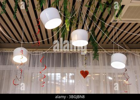 Hängende weiße Pendelleuchten, die mit roten Streulichtern, Grün und herzförmigen Ornamenten verziert sind, schaffen eine festliche Valentinstag-Atmosphäre. Stockfoto