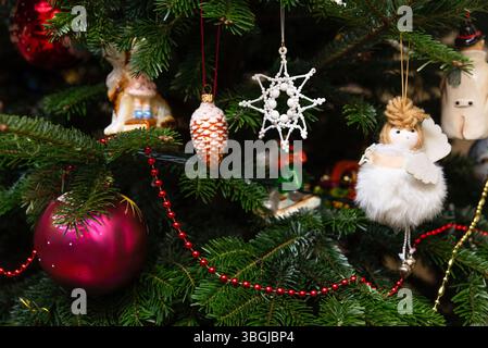Nahaufnahme eines geschmückten Weihnachtsbaums mit verschiedenen Ornamenten, darunter ein flauschiger Engel, Tannenzapfen, Stern und Kugeln. Stockfoto