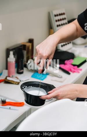 Nahaufnahme eines Friseurs, der Haarfärbemittel in einem Salon vorbereitet und Farblösung in einer schwarzen Schüssel an einem Arbeitsplatz mischt. Stockfoto
