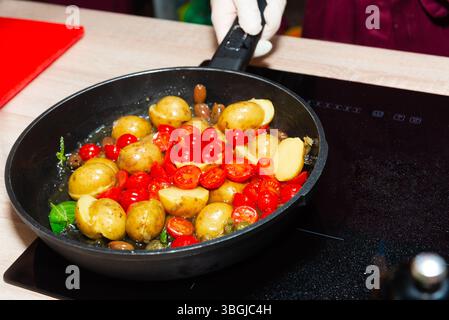 Bunte Pfanne mit sautierten Babykartoffeln, Kirschtomaten und Oliven, die mit Kräutern in Olivenöl auf dem Herd gekocht werden. Stockfoto