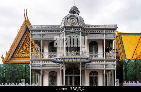 Ein atemberaubender architektonischer Blick auf ein historisches Gebäude mit aufwändigen Eisenarbeiten, Balkonen und einem Uhrenturm, umgeben von üppigem Grün und Tradi Stockfoto