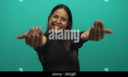 Frau dehnt Arme und umarmt sich in einem isolierten Studio als junges lateinamerikanisches Modell über grünem Hintergrund. Stockfoto