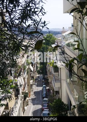 Blick von oben auf eine ruhige Stadtstraße in Athen, Griechenland, eingerahmt von weißen Gebäuden und geparkten Autos. Nur redaktionelle Verwendung. Stockfoto