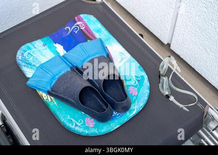 Ausrüstung für den Unterricht im professionellen Schwimmen. Flossen, Brille und ein mit Staub bedecktes Schwimmbrett liegen auf einem zusammengesetzten Liegestuhl und warten auf die Sportse Stockfoto