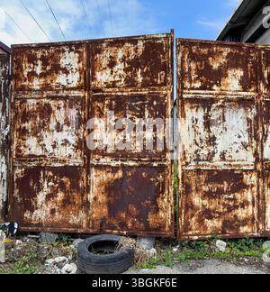 Alte, rostige Metalltore mit Korrosion, abblätternder Farbe und urbanem Schmutz auf dem Boden. Geeignet für Textur, Zerfall, urbane Hintergründe und Grunge-Design. Stockfoto