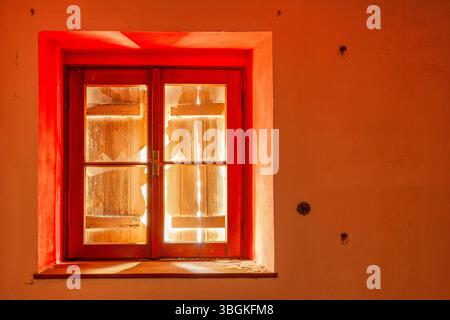 Altes rotes Fenster mit Rollenverschluss auf verlassenem alpinen Gebäude, mit gefiltertem Licht durch Holzrisse Stockfoto