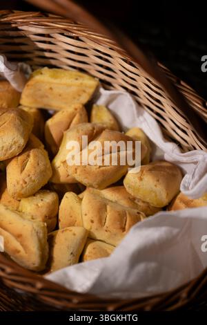 Ein detailliertes Nahfoto von frisch gebackenen paraguayischen Chipas, die in einem rustikalen Webkorb angeordnet sind. Das Bild hebt die goldene, käsige Textur o hervor Stockfoto