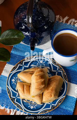 Ein Blick von oben auf ein traditionelles paraguayisches Frühstück mit einem Teller Chipas, einer Emailtasse gefüllt mit Cocido und einem dunkelblauen Wasserkocher. Die Rusti Stockfoto
